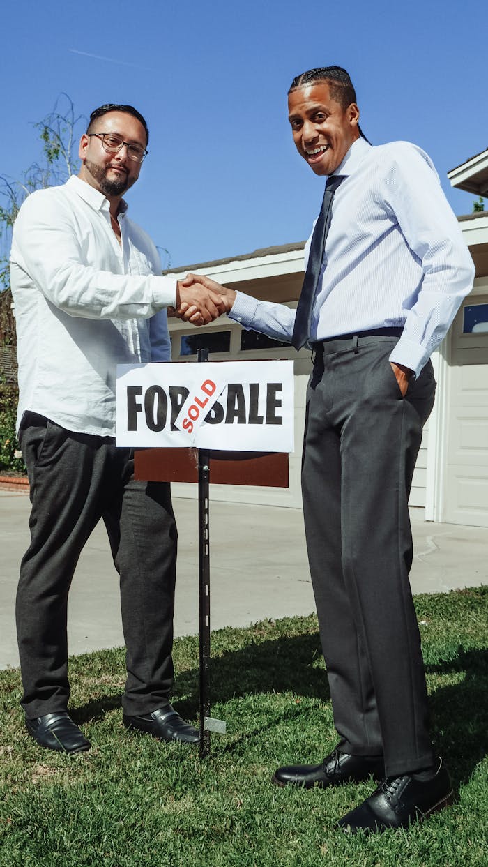 services-01 Two men shaking hands in front of a house with a sold sign, marking a successful real estate deal.