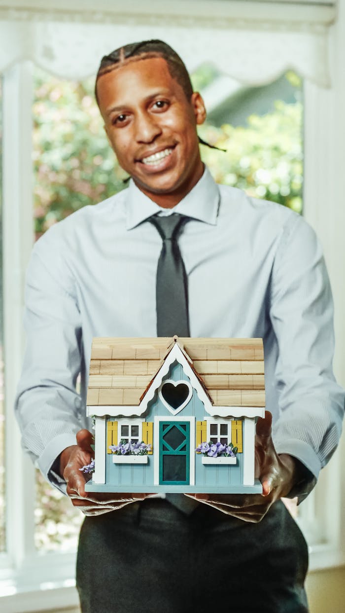 gallery-2 Smiling agent presents a charming miniature house, symbolizing real estate opportunities.