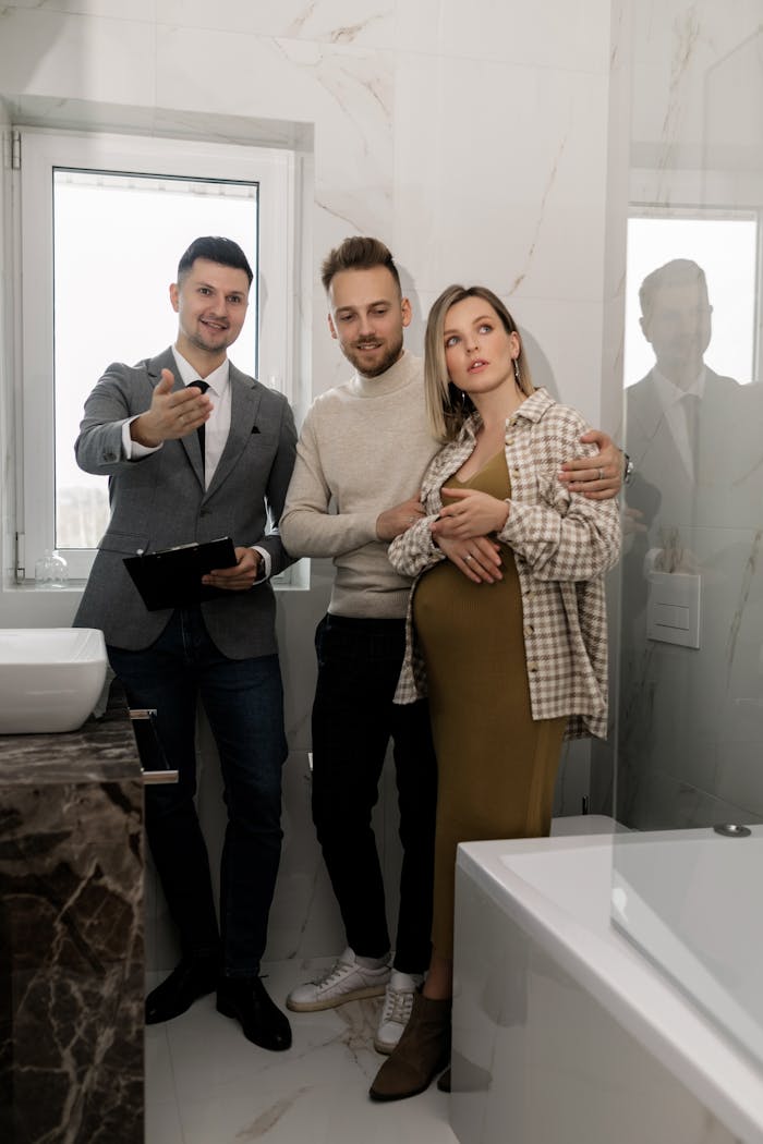 services-02 A real estate agent shows a modern bathroom to an expectant couple considering a home purchase.